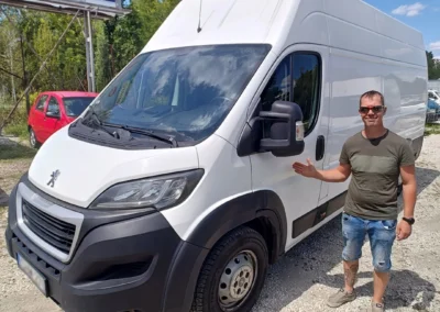 Peugeot Boxer L4H3 furgon bal elölről, fehér. Mellette áll Zoli napszemüvegven